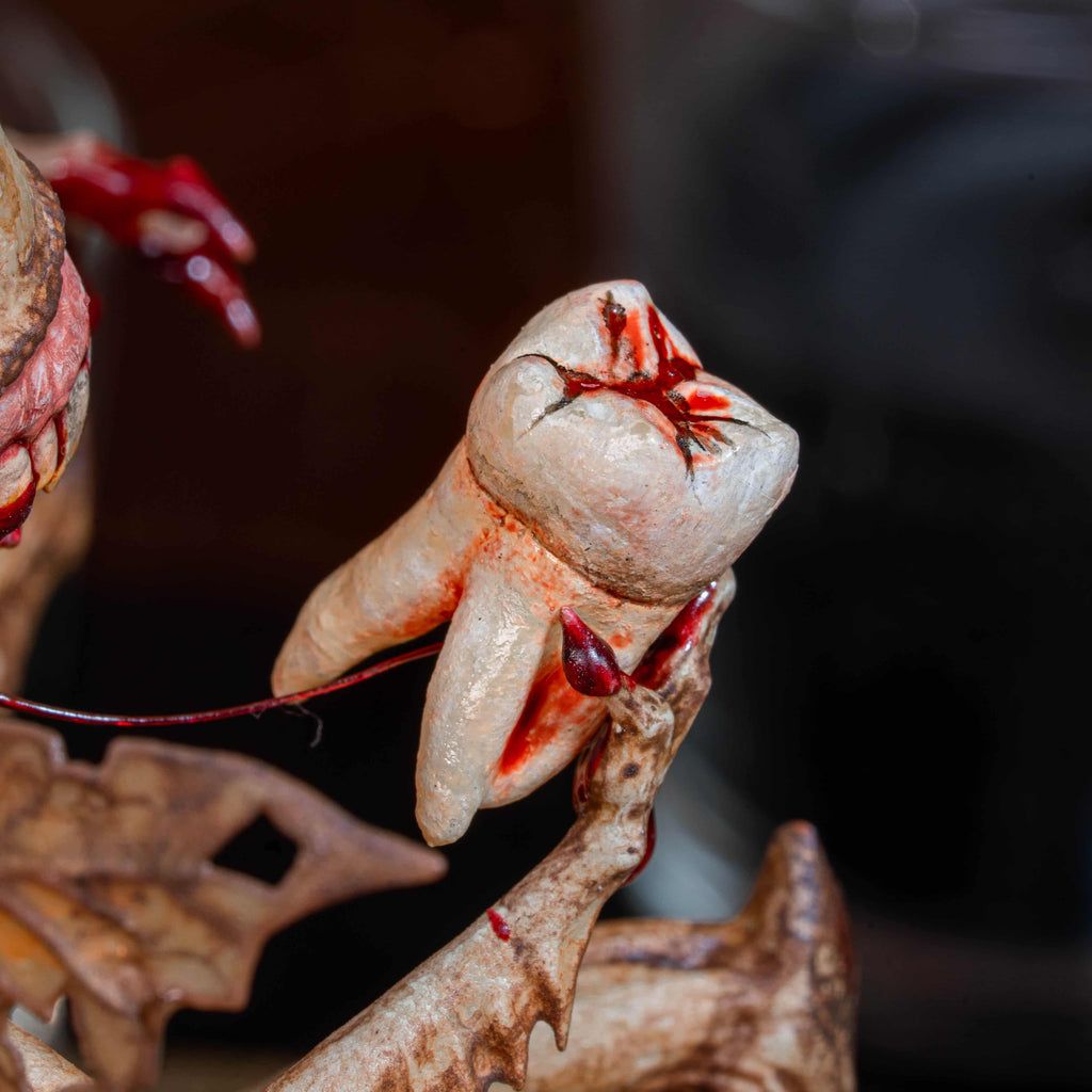 3D printed Tooth Fairy Hellboy figurine with skeletal wings, sharp claws, and a grotesque grin holding a tooth, surrounded by scattered white teeth. Hand-painted in bone, red, and brown tones, this dark fantasy collectible doubles as a tooth holder, making it perfect for gothic decor, horror props, or a unique keepsake for children’s lost teeth.