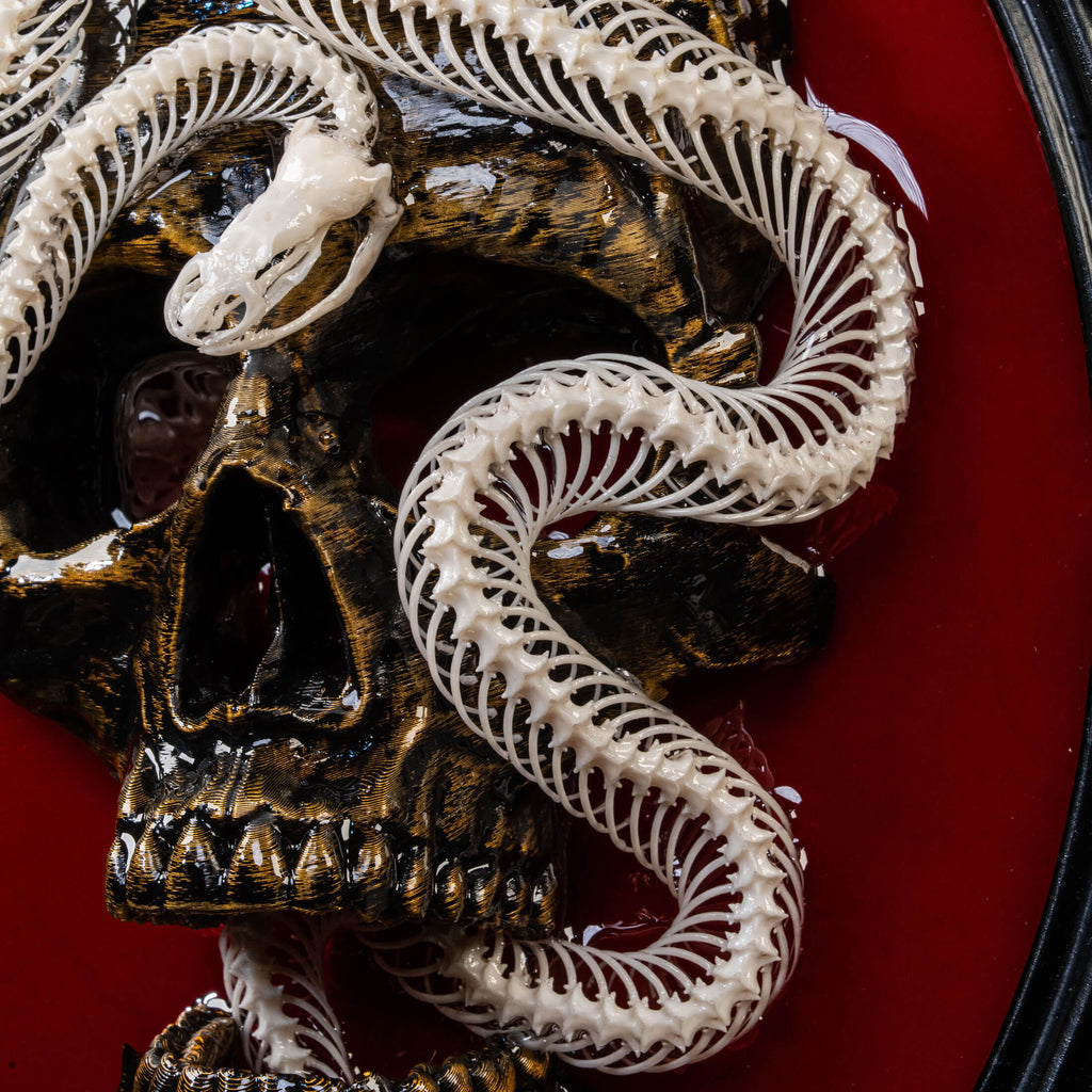 May include: A white snake skeleton coiled around a gold skull on a red background. The snake skeleton is detailed and realistic, with visible vertebrae and ribs. The skull is also detailed, with visible teeth and eye sockets.